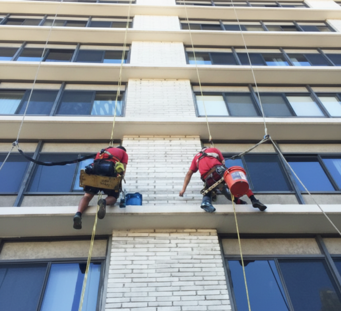 Technicians performing exterior window cleaning on a tall commercial building